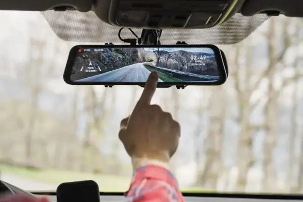 Driver using a touchscreen mirror dash cam mounted on a car windshield showing rear road view